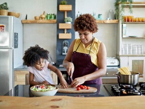 mulher pica legumes sob mesa de cozinha com criança ao lado interagindo mulher pica legumes sob mesa de cozinha com criança ao lado interagindo