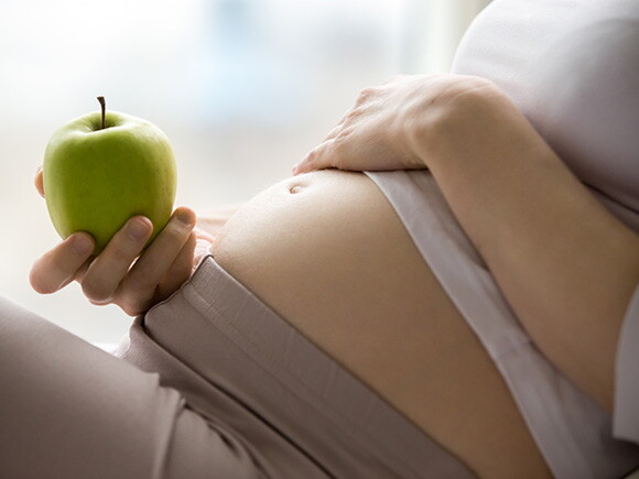Foto de mulher grávida segurando maçã.