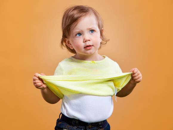 bebe menina de tres anos com blusa amarela no fundo laranja