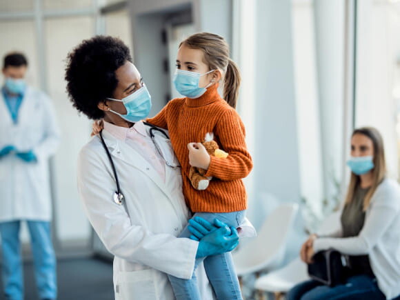 médica sorrindo enquanto segura uma criança em um ambiente hospitalar