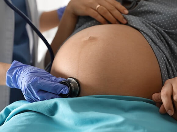 Médico com estetoscópio examinando mulher grávida para garantir a saúde da mãe e do bebê