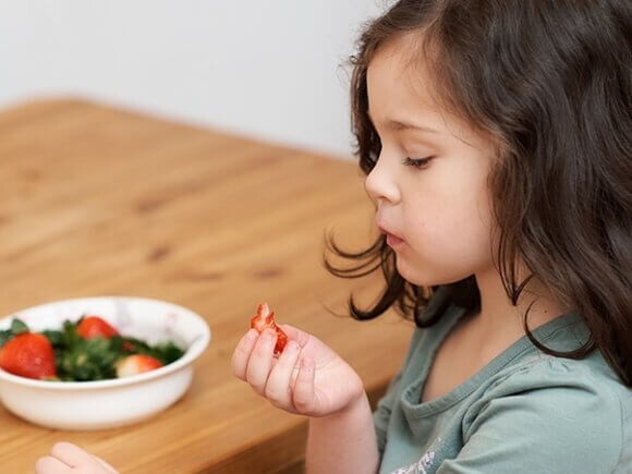 Criança pegando um alimento que está no prato na sua frente 