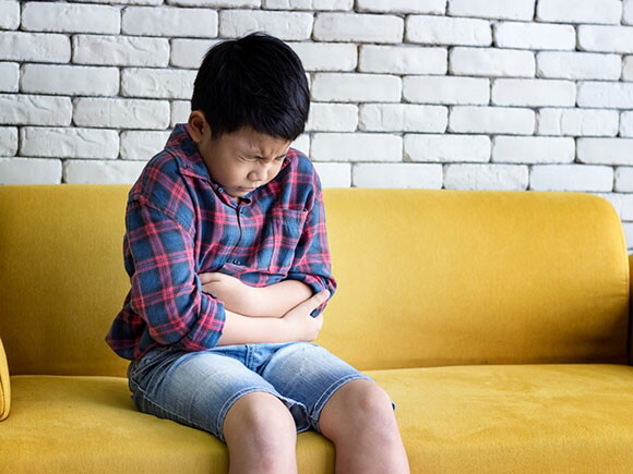 menino sentado no sofá com feição de dor abraçando a barriga