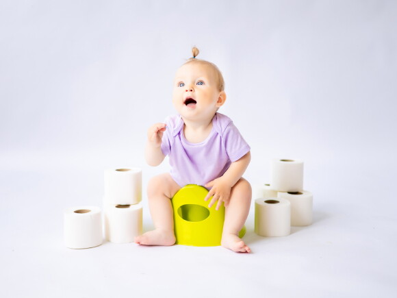 Foto de bebê sentada no penico rodeado por rolos de papel higiênico