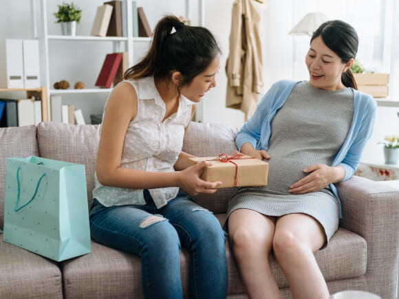 mulher grávida sentada no sofá recebe presentes de amiga em chá de fraldas