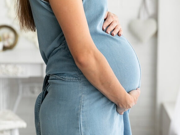 Mulher grávida de perfil com as mãos sobre a barriga