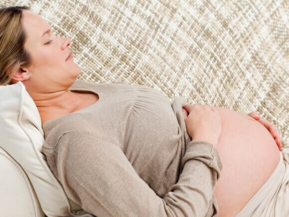 Mulher grávida deitada no sofá embalando sua barriga