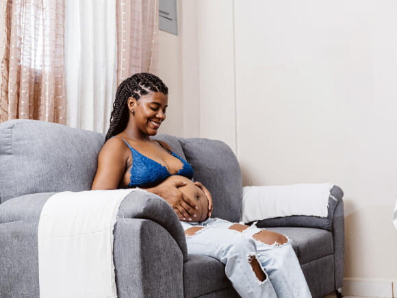 mulher grávida sentada ao sofá enquanto sente contração do bebê