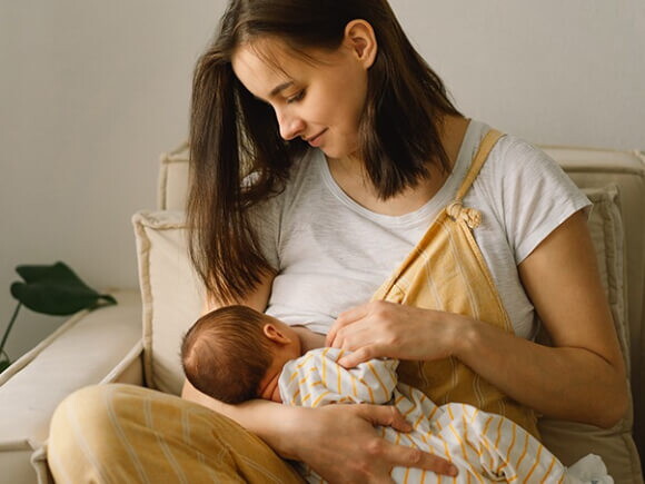 mulher sentada amamentando bebê que está no seu colo