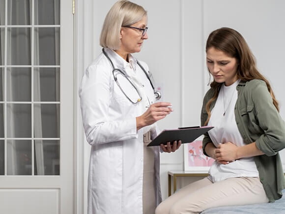 Mulher sentada em uma cama de hospital discutindo sua condição médica com uma profissional de saúde