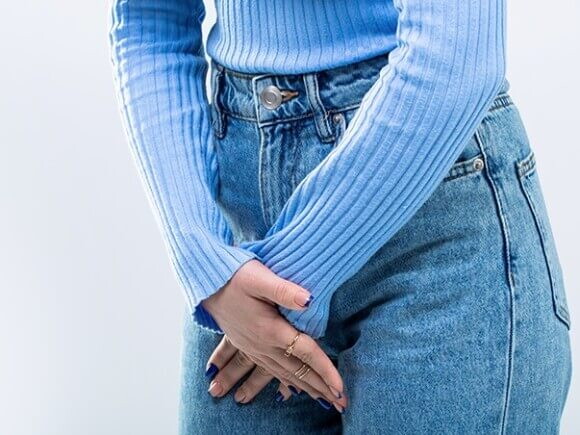 mulher usando calça jeans com as mãos posicionadas à frente da região íntima feminina