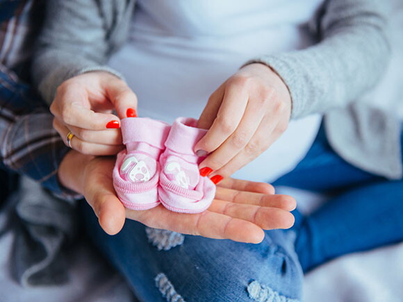 mulher grávida segura um par de sapatinhos rosas de bebê 