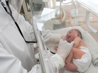 Bebê em uma incubadora sendo examinado por um médico