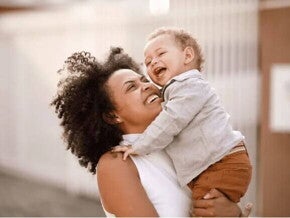 Mãe sorridente carrega o filho no colo, ilustrando a fase conhecida como terrible two. 