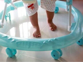 Pés de um bebê em um andador azul, sobre piso claro, mostrando o equipamento em uso.