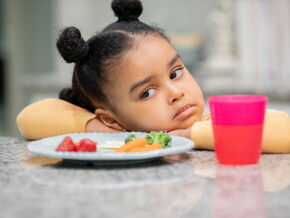 menina com semblante desconfiado olha para prato de comida sem vontade
