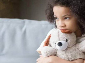Imagem de uma criança sozinha segurando um bicho de pelúcia, olhando de forma distraída para o nada, este olhar pode ser um sintoma de síndrome de asperger