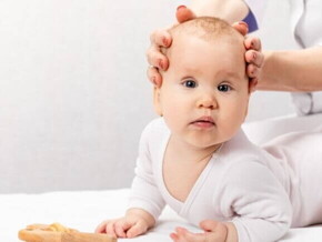 Um bebê deitado com a sua cabeça sendo segurada por duas mãos Um bebê deitado com a sua cabeça sendo segurada por duas mãos