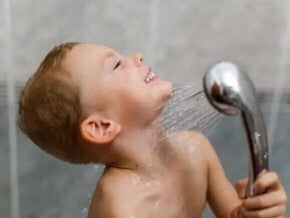 Um menino toma banho sozinho, exercitando sua autonomia infantil, com a ajuda de uma ducha móvel. 