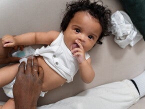 bebê de fralda e body branco, com a mão de adulto sobre a barriga
