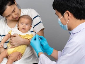imagem de um bebê no colo de uma mulher adulta e um homem segurando uma seringa, vestindo roupas de profissionais da saúde na cor branca imagem de um bebê no colo de uma mulher adulta e um homem segurando uma seringa, vestindo roupas de profissionais da saúde na cor branca