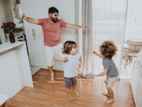 Pai e filhos pequenos brincam desenvolvendo a coordenação motora grossa dentro de casa.
