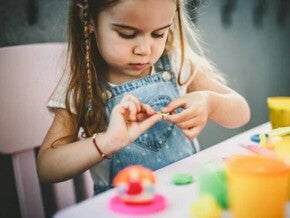 A foto mostra uma criança brincando de massinha de modelar e estimulando a coordenação motora fina