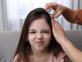 Menina com rosto irritado recebendo uma medicação no couro cabeludo