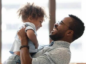 Uma criança é carregada pelo seu pai. Os dois estão brincando e sorrindo. A imagem remete ao tema crise dos três anos Uma criança é carregada pelo seu pai. Os dois estão brincando e sorrindo. A imagem remete ao tema crise dos três anos
