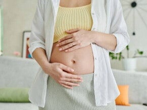Uma mulher grávida em pé, com as duas mãos sobre a barriga.