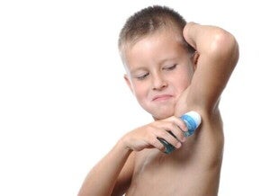 Menino utilizando um desodorante em formato roll-on sob um fundo branco.