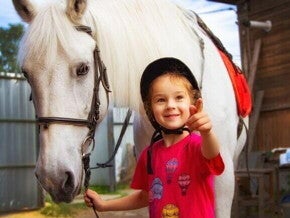 Menina sorrindo e apontando com o dedo, enquanto segura a rédea de um cavalo
