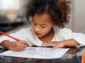 menina debruçada sobre mesa fazendo desenho