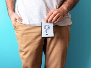 Homem de camiseta branca e calça marrom segurando um papel desenhado um ponto de interrogação em frente ao seu órgão genital Homem de camiseta branca e calça marrom segurando um papel desenhado um ponto de interrogação em frente ao seu órgão genital