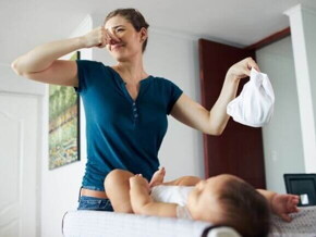 Uma mulher em pé, segurando uma fralda em uma mão e tapando o nariz com a outra mão, com um bebê deitado em sua frente Uma mulher em pé, segurando uma fralda em uma mão e tapando o nariz com a outra mão, com um bebê deitado em sua frente