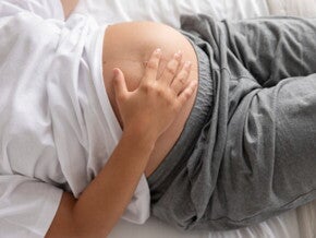gestante deitada com a mão na barriga proeminente de gestação avançada