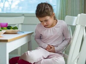 Menina com intoxicação alimentar, sentada à mesa de jantar, reagindo à dor, colocando as mãos na barriga