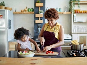 mulher pica legumes sob mesa de cozinha com criança ao lado interagindo