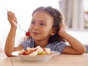 Representando bons hábitos alimentares, uma criança come seu lanchinho: várias frutas picadas em um prato. 