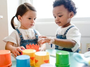 imagem de duas crianças pequenas vestindo macacão jeans e camiseta branca, brincando com brinquedos pedagógicos.