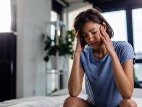 mulher com as mãos sob a cabeça e com expressão de dor
