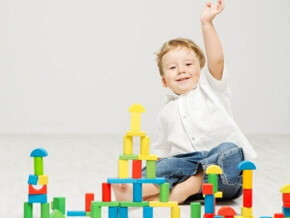 Um bebê sentado no chão com a mão para cima, em frente de diversos blocos coloridos de construir.
