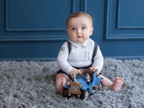 bebê menino sentado em tapete felpudo cinza, com carrinho de brinquedo azul em mãos.