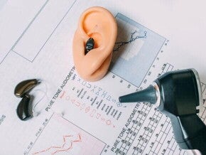 Diversos aparelhos voltados à saúde auditiva, dispostos em cima de um resultado de exame de audiometria