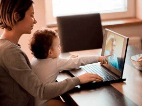 Ilustrando a separação dos pais, uma mãe segura um bebê em seu colo. Eles estão sentados à mesa em frente ao computador. O bebê aponta para a tela, onde há um homem por videochamada.