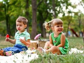 Piquenique infantil Um menino e uma menina estão sentados em uma toalha em um parque. Sobre ela temos algumas cestas e lanchinhos. O cenário todo remete muito a um dia de piquenique