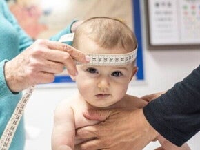 Profissionais de saúde medem a circunferência da cabeça de um bebê utilizando uma fita métrica, durante uma consulta de acompanhamento do desenvolvimento infantil.