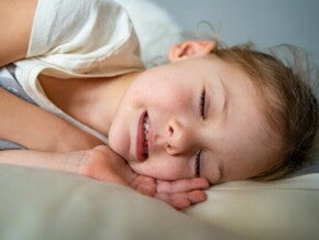 Uma criança dormindo, com um leve sorriso e os dentes visíveis.