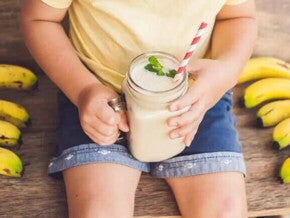 criança sentada ao redor de algumas bananas, segurando vitamina