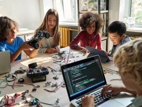 Grupo de crianças sentadas em uma mesa com várias ferramentas tecnológicas.